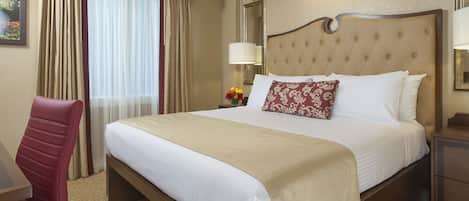 A hotel room with a large bed, a desk, a chair, and a nightstand.
