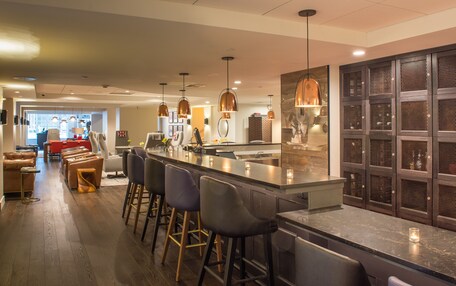 A modern kitchen with a bar area, featuring a long counter, bar stools, pendant lighting, and a view into the dining area.