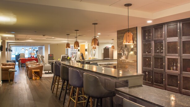 Une cuisine moderne dotée d’un coin bar, comprenant un long comptoir, des tabourets de bar, un éclairage suspendu et une vue sur la salle à manger.