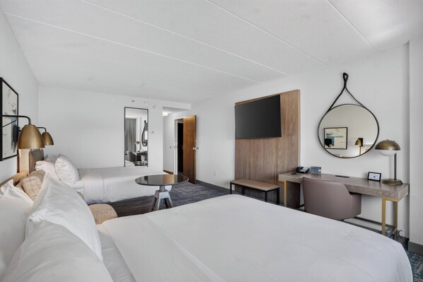A hotel room with a large bed, a desk, a chair, a TV, and a mirror.