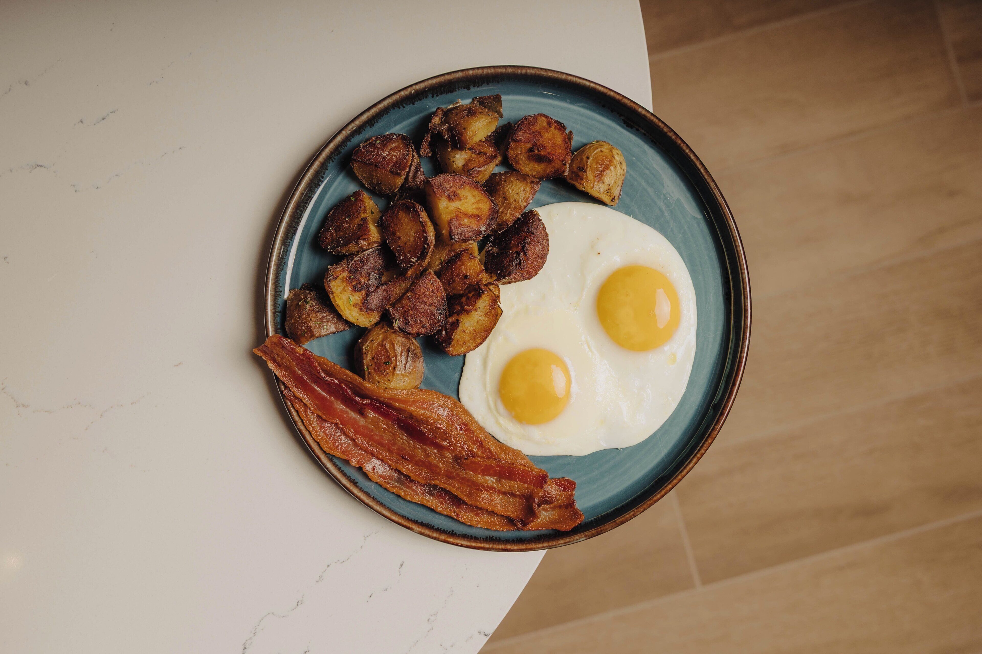 Um prato com ovos fritos, bacon e batatas assadas.