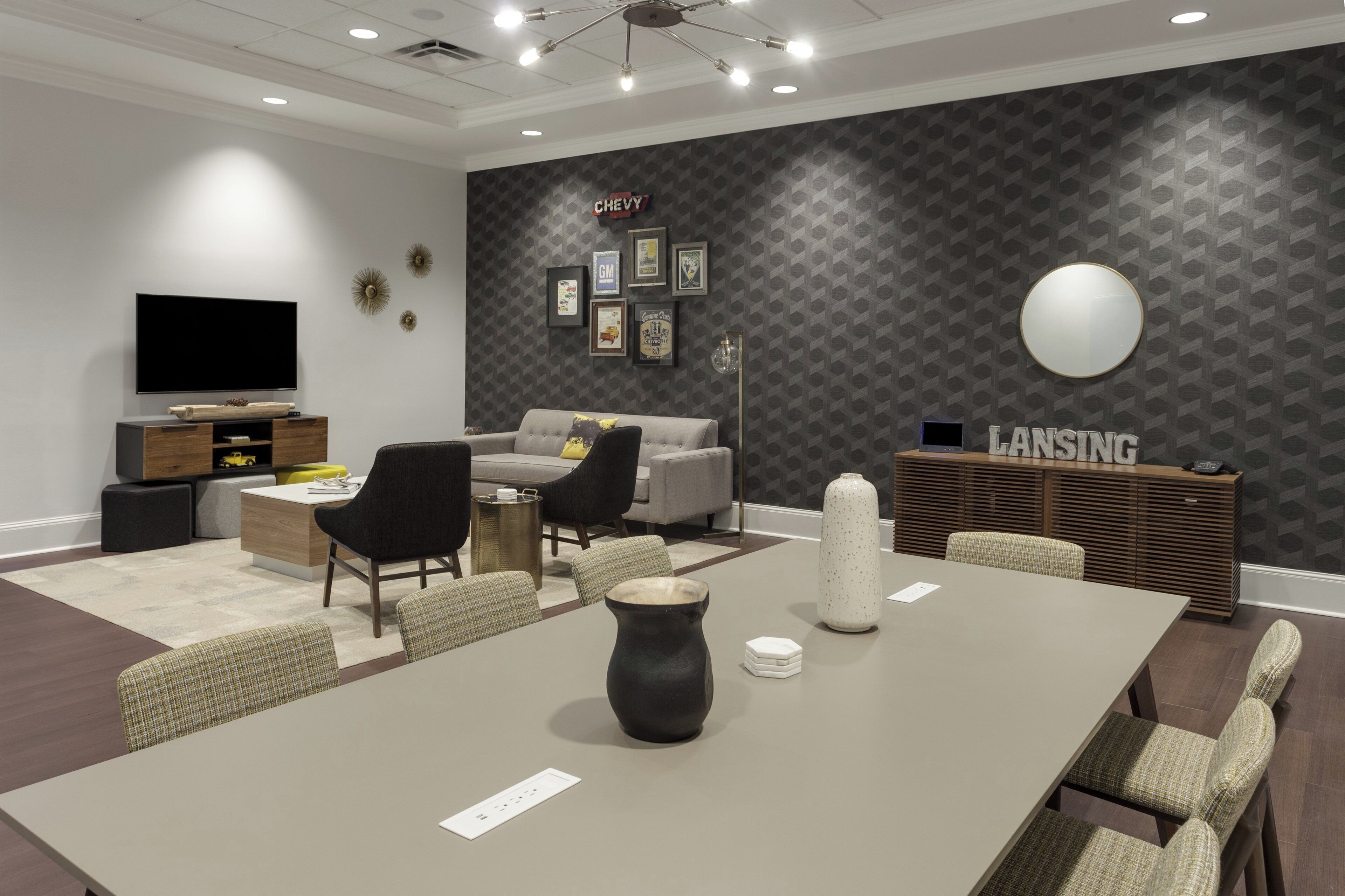 A modern conference room with a large table, chairs, a television, and a wall with Chevrolet memorabilia.