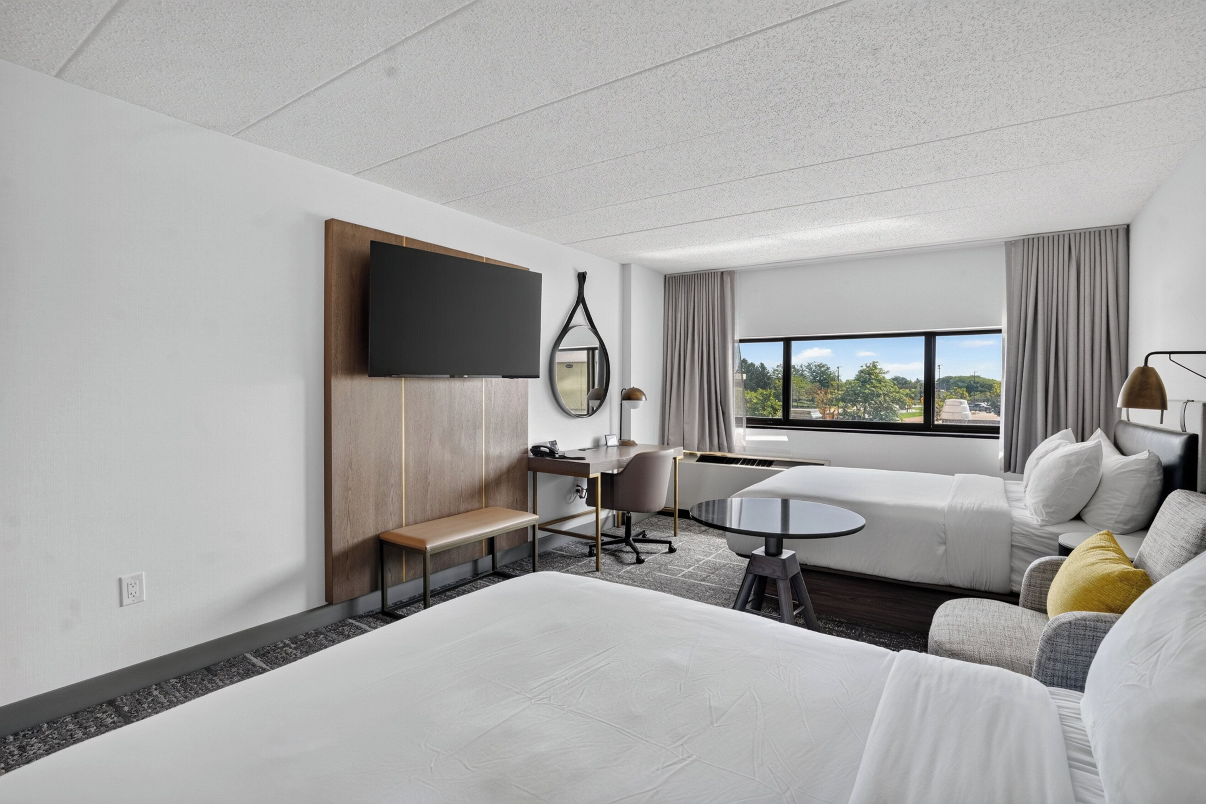 A hotel room with a bed, a desk, a chair, a sofa, a small table, a TV, and a window with a view.