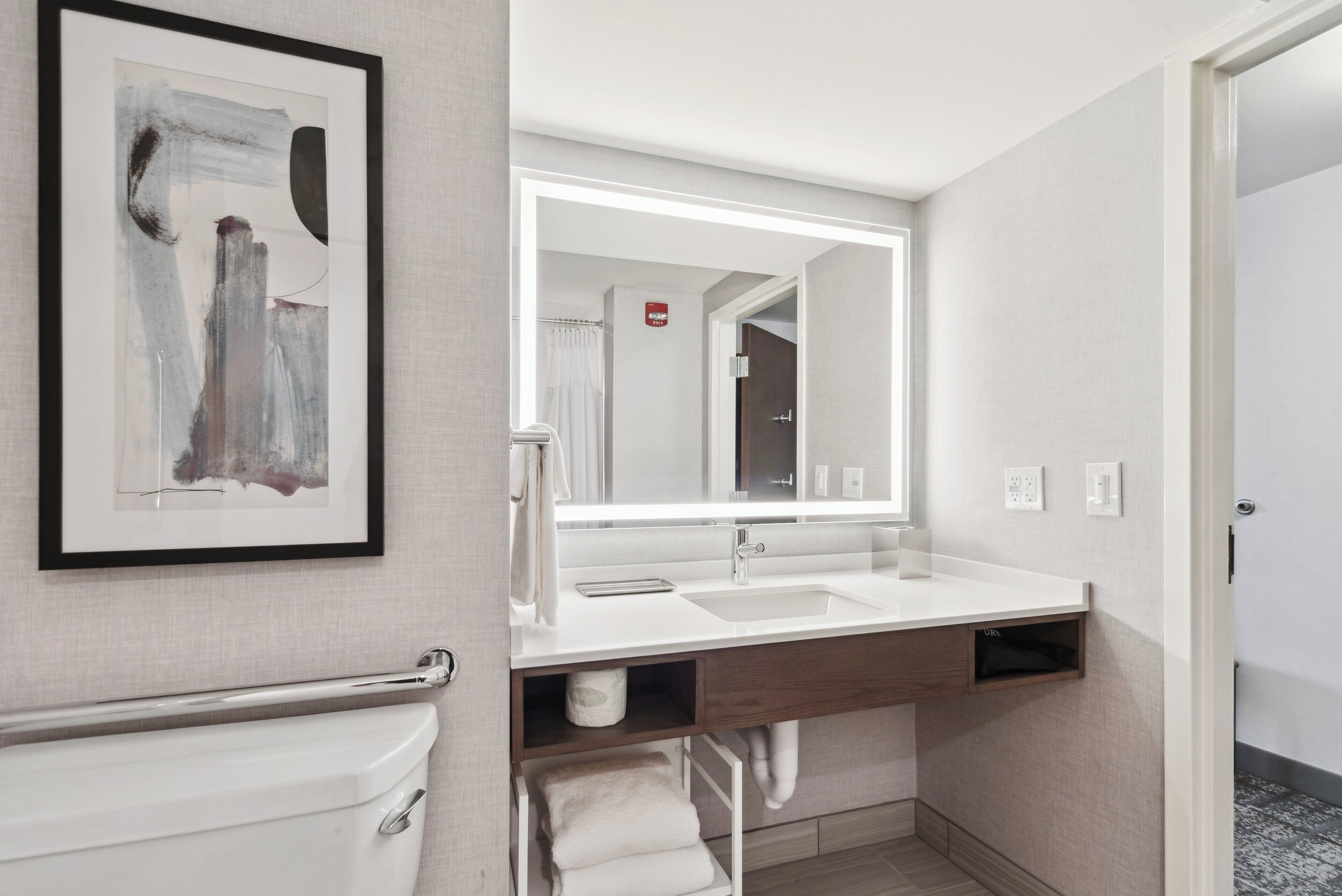 A modern bathroom with a white sink, a large mirror, and a framed abstract painting.