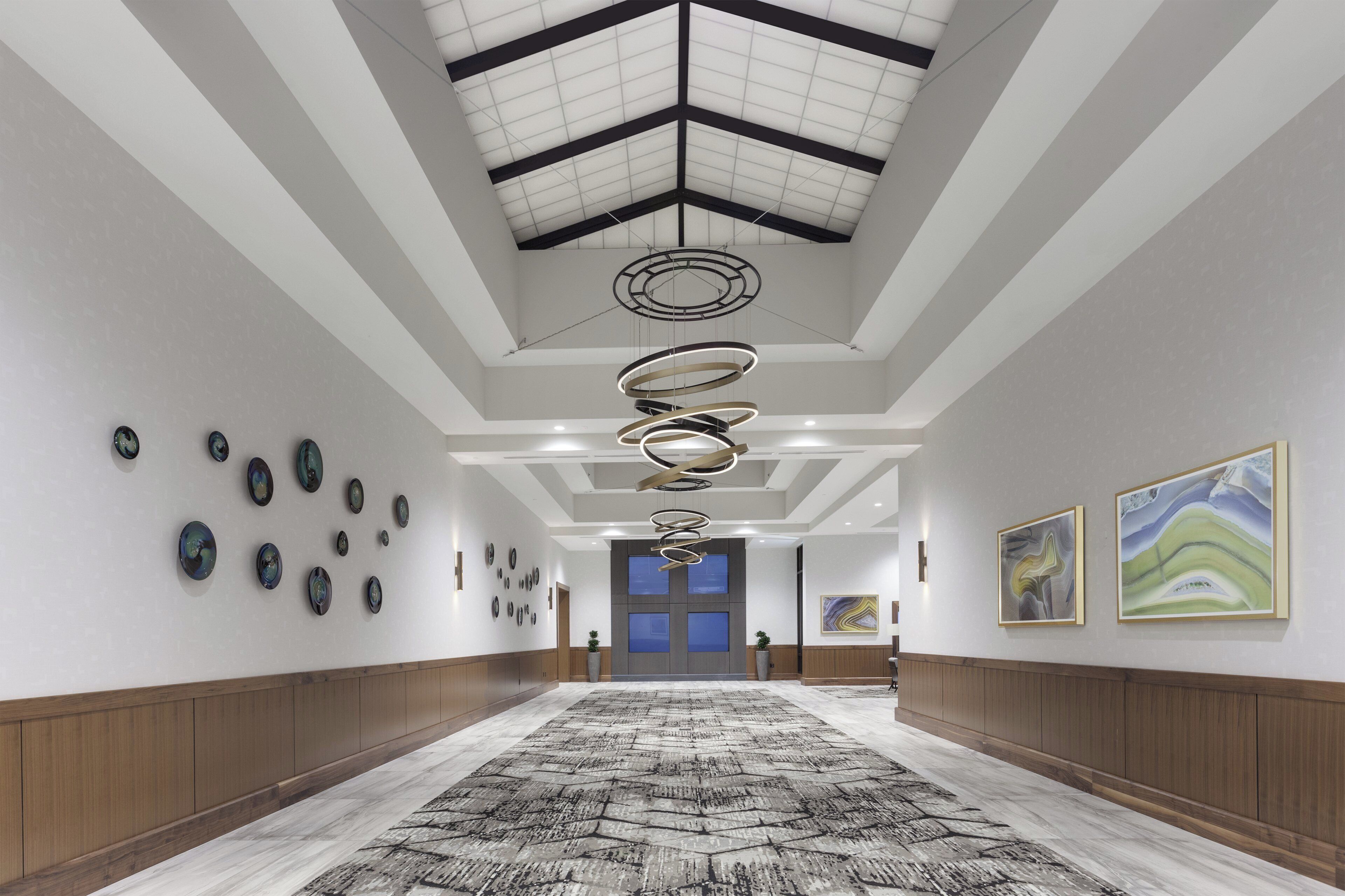 Een gang met een gekleurd tapijt, een plafond met een geometrisch patroon en ronde decoraties aan de muur.