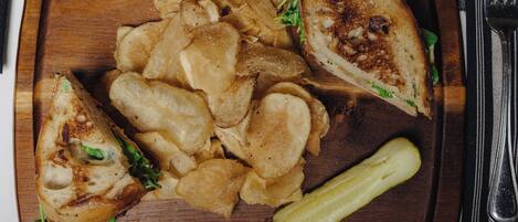 A wooden serving tray with a grilled sandwich, potato chips, and a pickle.