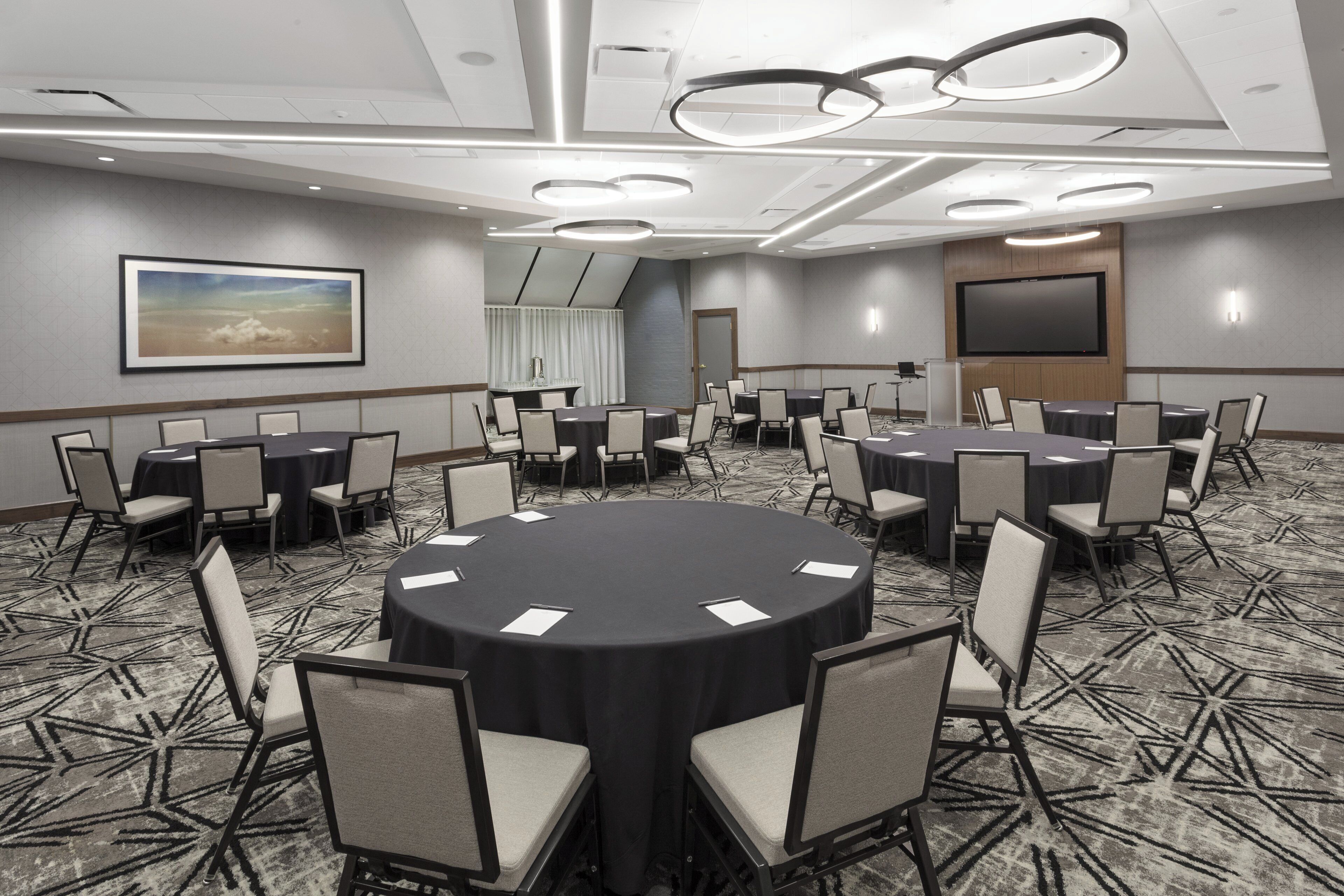 A conference room with round tables and chairs, a large screen, and a painting on the wall.