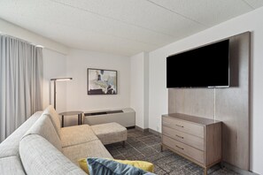 A modern living room with a sofa, ottoman, and a flat-screen TV mounted on the wall. - Crowne Plaza Lansing by IHG (Lansing)