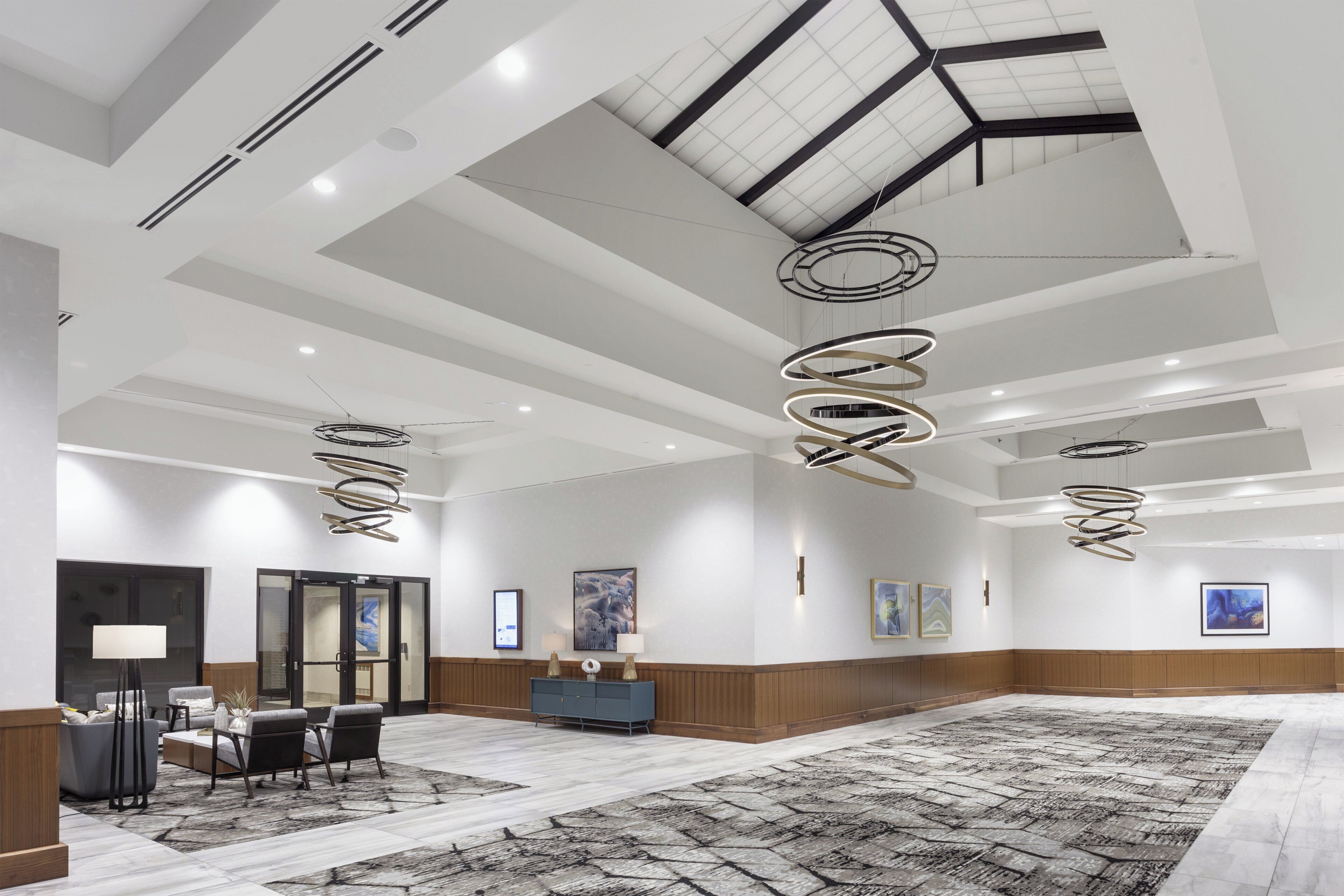 A spacious hotel lobby with a high ceiling, modern lighting fixtures, and a large seating area.