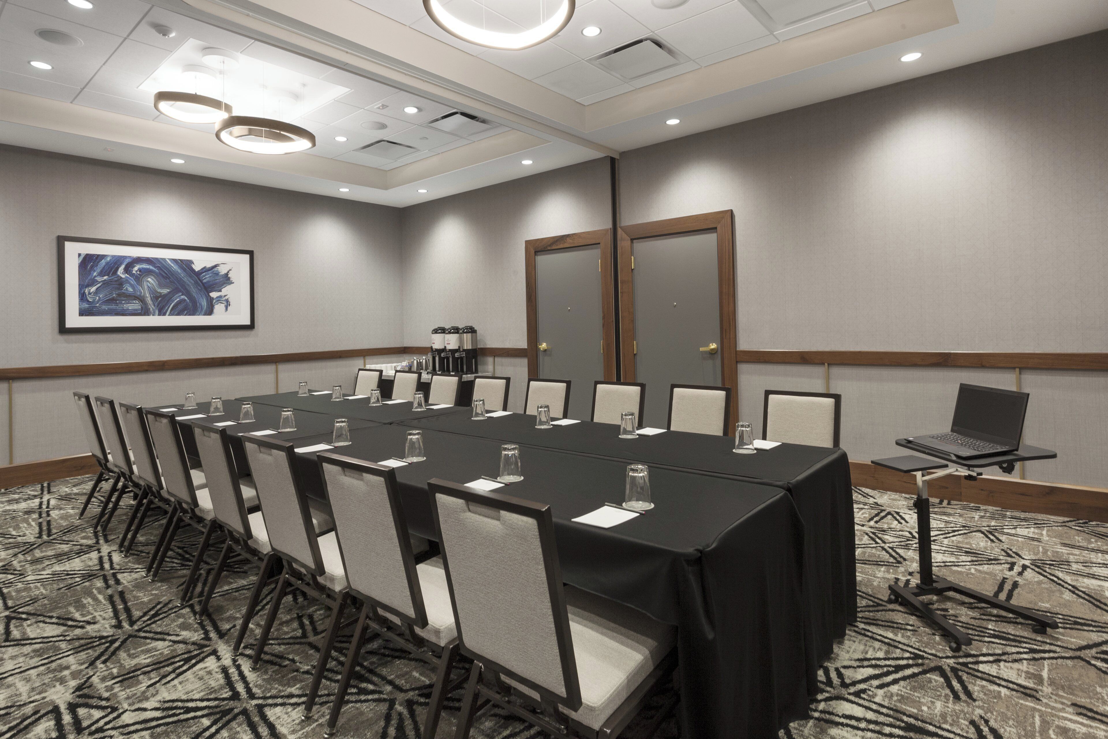 A conference room with a long table, chairs, a coffee station, and a laptop on a stand.