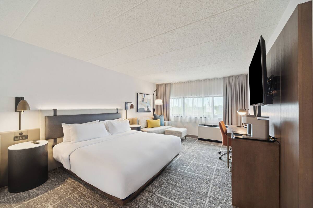 A hotel room with a large bed, a desk, a TV, and a window with curtains.