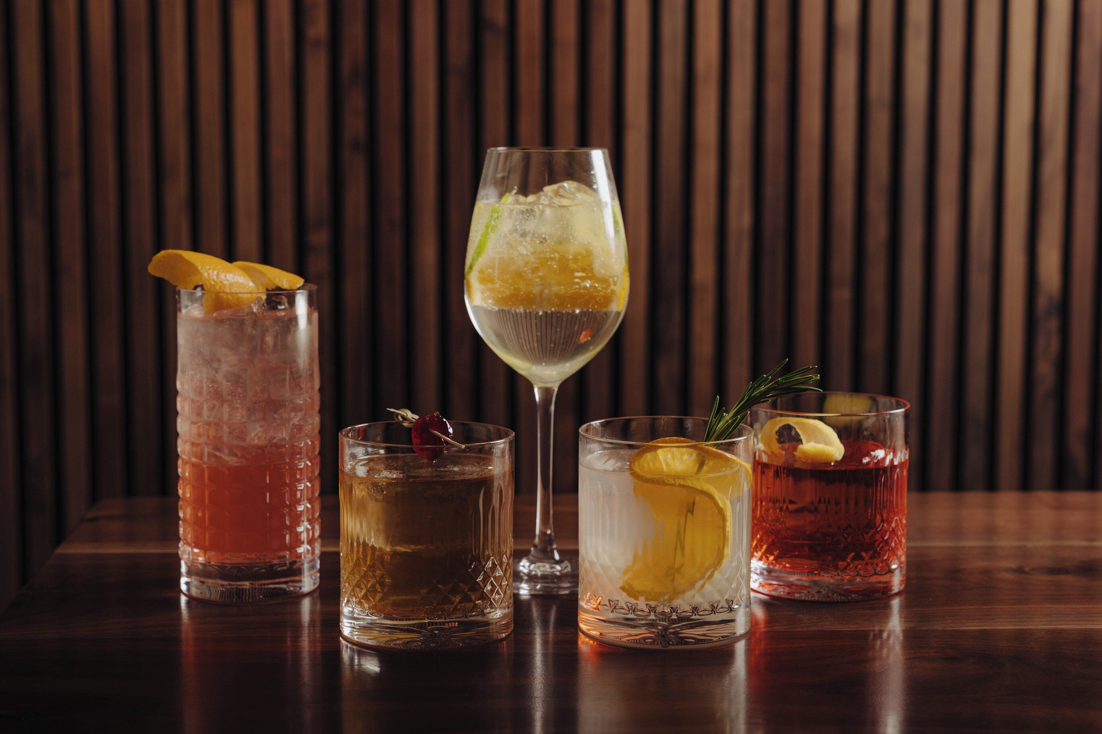 Four glasses of different beverages on a wooden table against a wooden background.