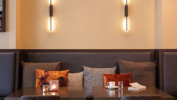 A modern hotel room with a dark-colored sofa set, a table with a candle, a cup, and a glass of water.