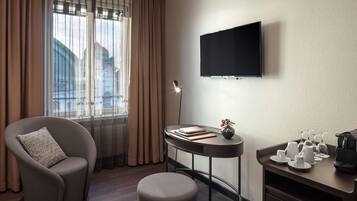 Una habitación de hotel moderna con un ventanal grande, un televisor de pantalla plana, un sillón cómodo, una mesita redonda con un florero y una estación de café.