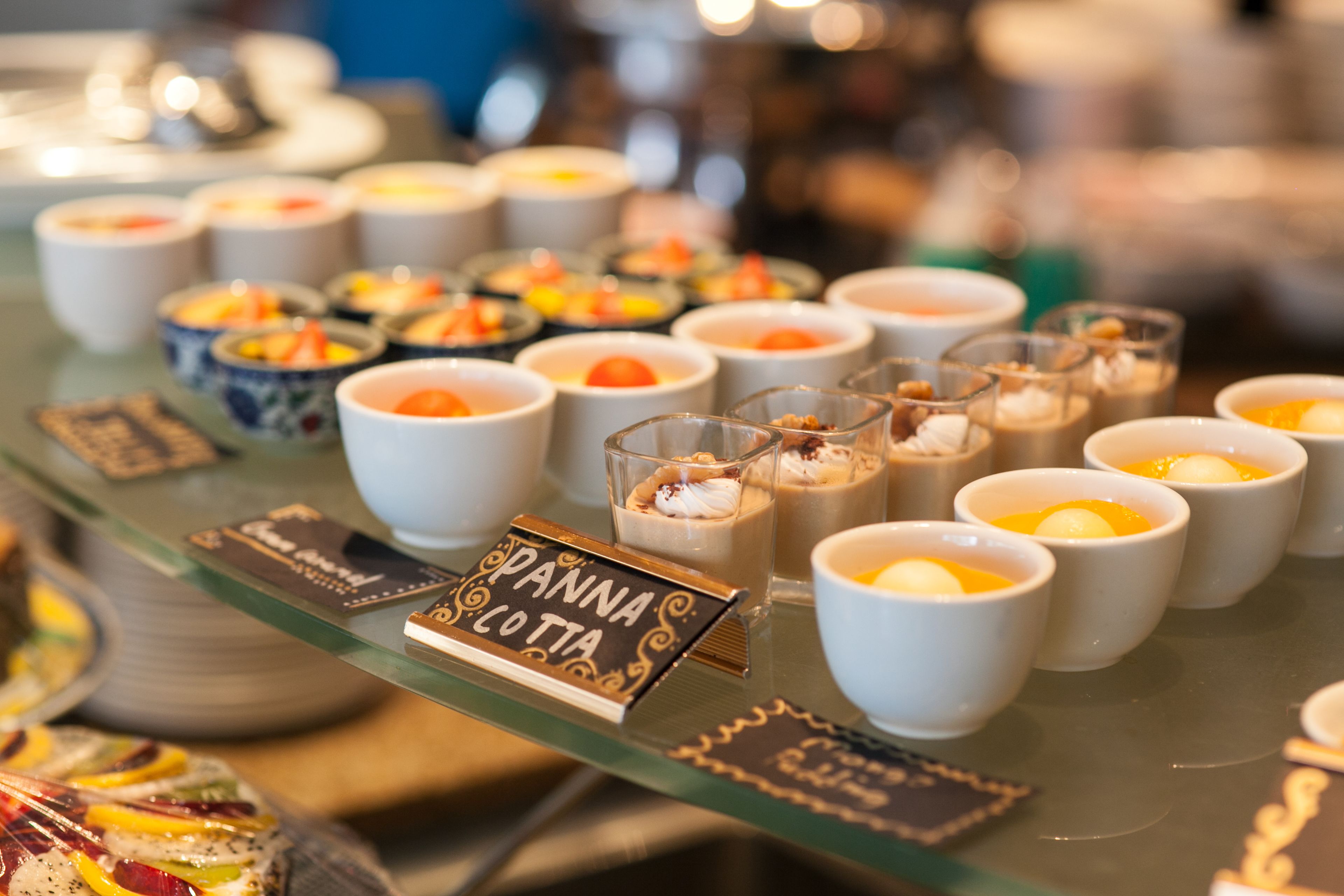 Diverse desserts in een glazen vitrine, waaronder panna cotta en andere lekkernijen.