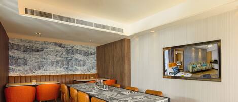 A modern dining area with a long table, orange chairs, and a patterned tablecloth.