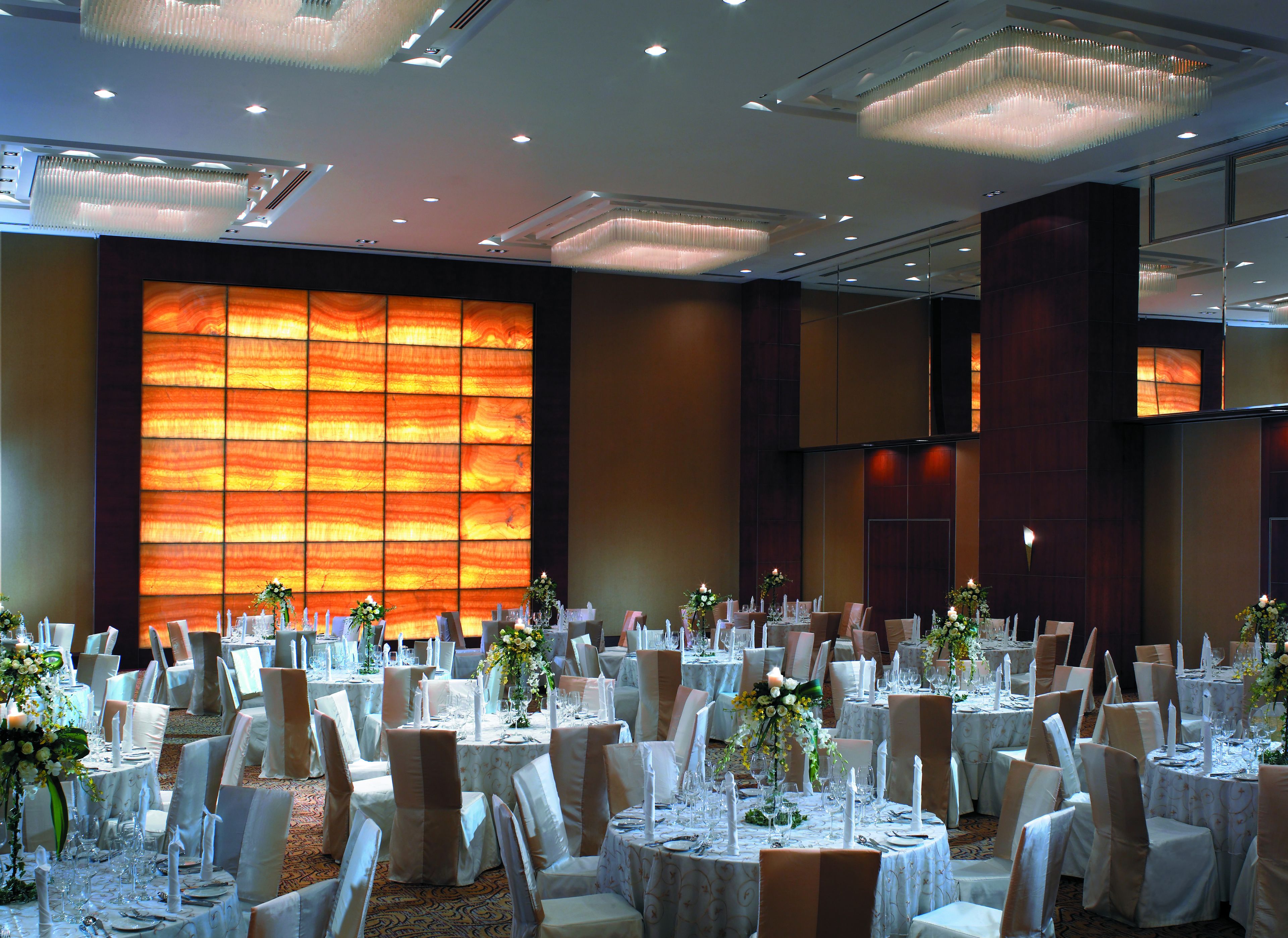 Une salle de banquet avec des tables rondes, des nappes blanches et des chaises ornées de rubans marron.