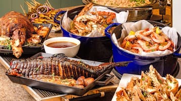 Diversos platos de mariscos, incluyendo un pescado entero asado, patas de cangrejo y camarones, presentados en una mesa de buffet.