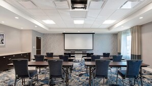 A conference room with a large screen, multiple tables, and chairs.