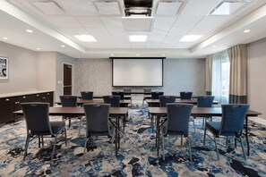 Une salle de conférence équipée d’un grand écran, de plusieurs tables et de chaises.