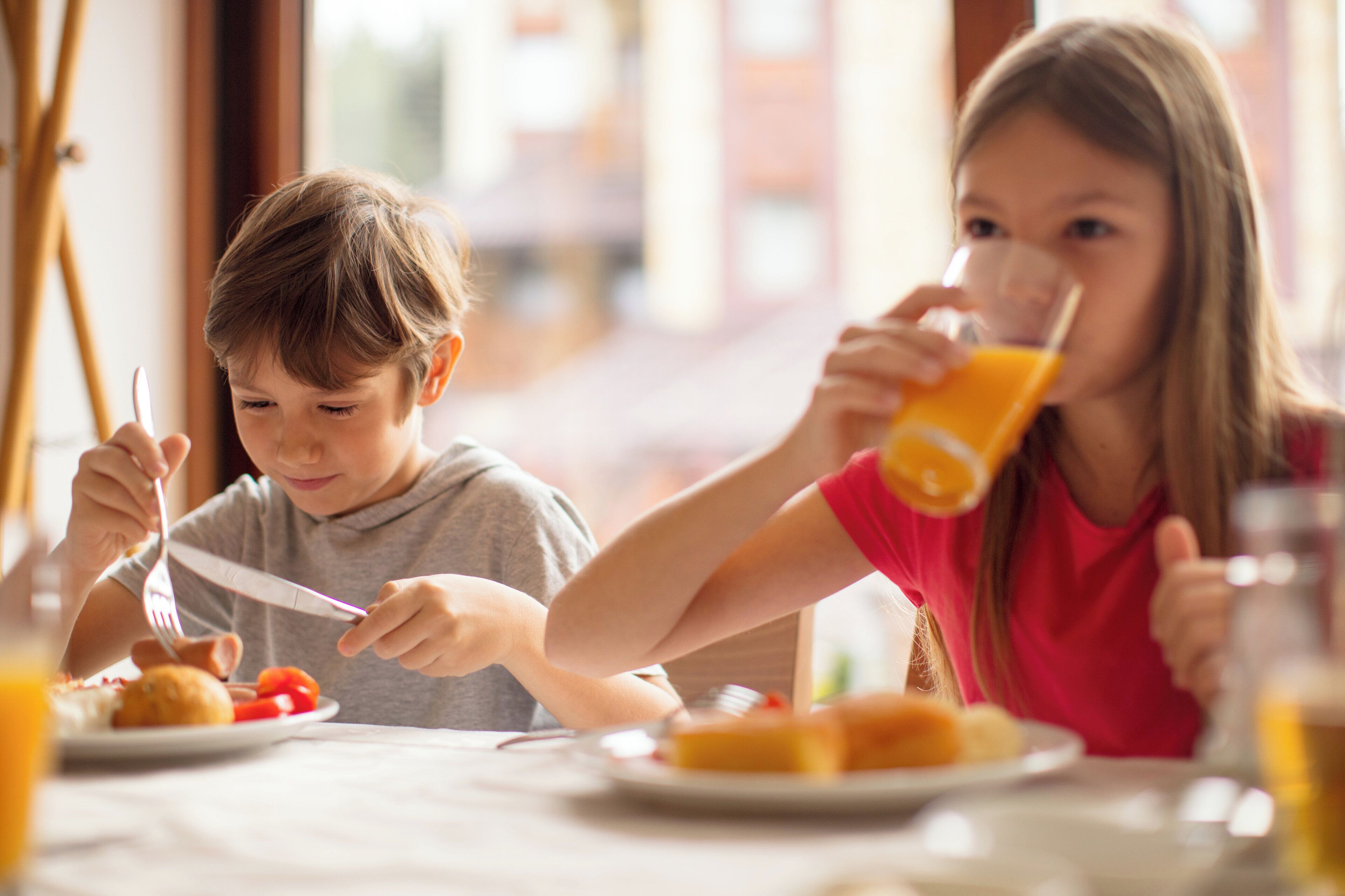 Two children eating breakfast at a table with plates of food and drinks.