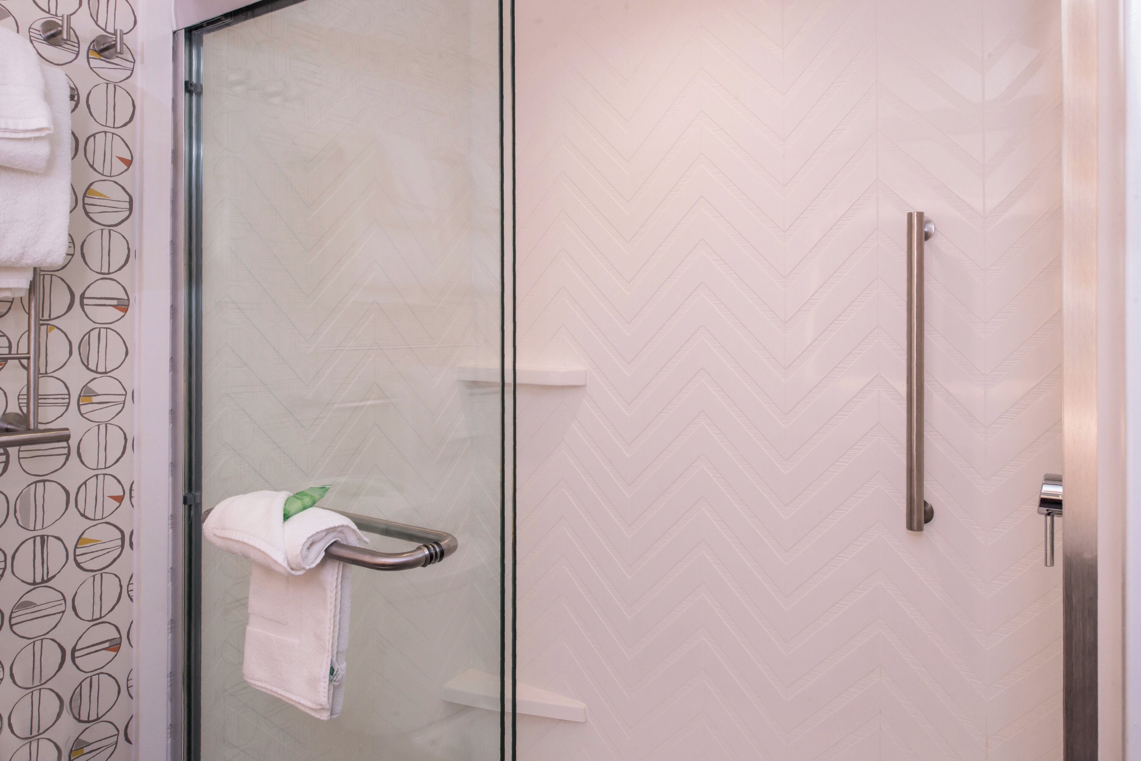 A bathroom with a glass door, a towel rack, and a herringbone-patterned wall.