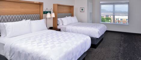 A hotel room with two beds, a large window, and a view of buildings.
