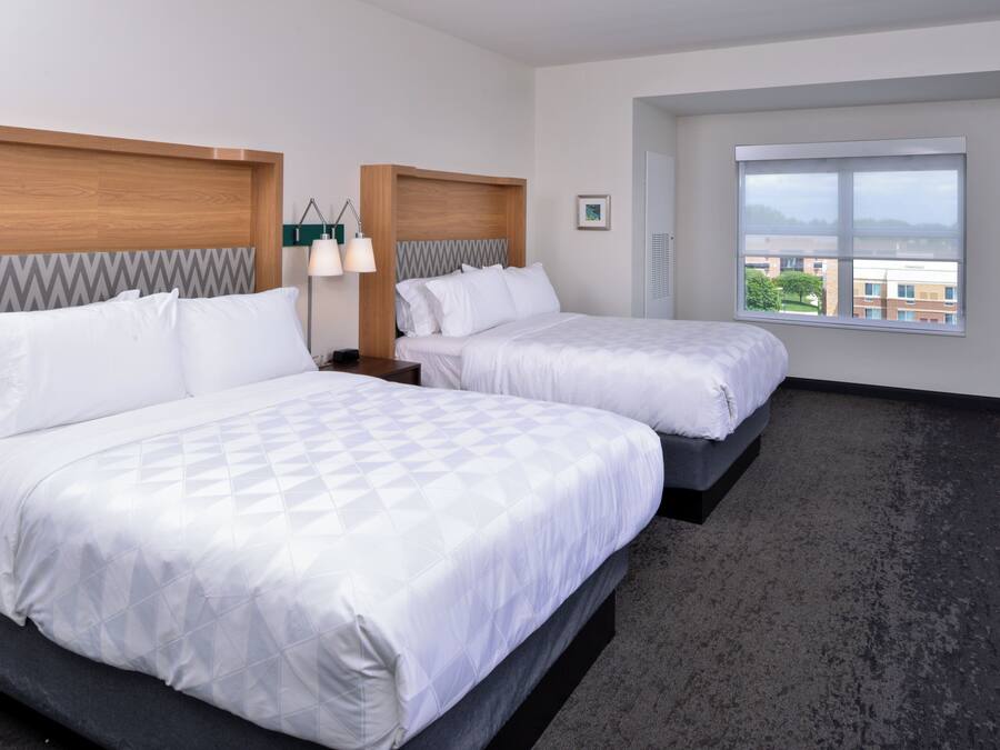 Habitación de hotel con dos camas, un ventanal grande y vistas a edificios.