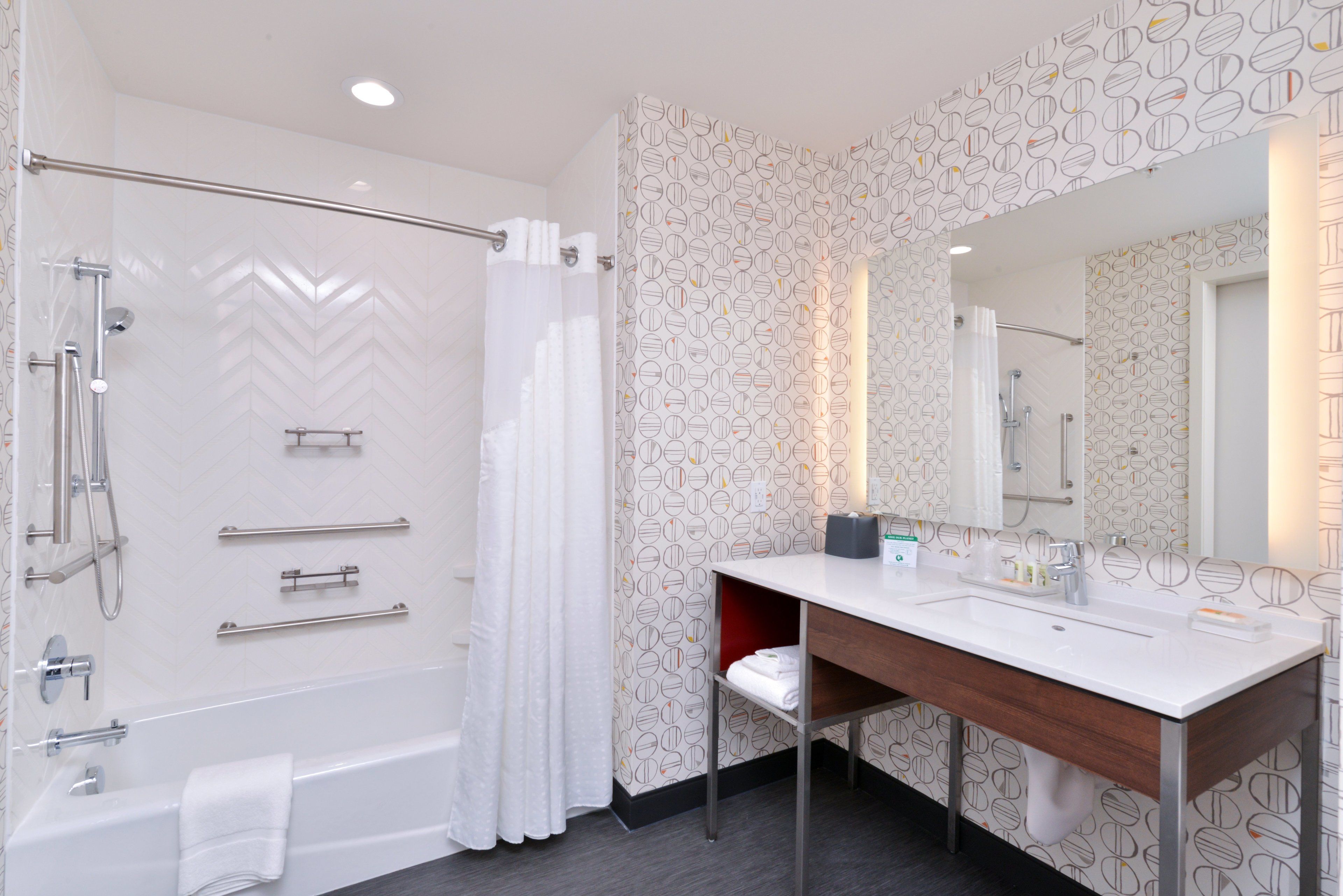Une salle de bain moderne équipée d’une douche, d’un meuble-lavabo avec miroir et d’un porte-serviettes.