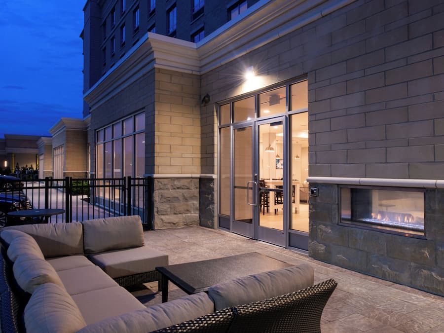 An outdoor seating area with a fire feature, a stone wall, and a glass door leading to an interior space.