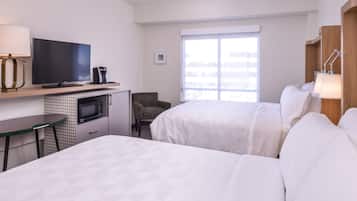 A hotel room with two beds, a desk with a flat-screen TV, a microwave, a chair, and a large window.