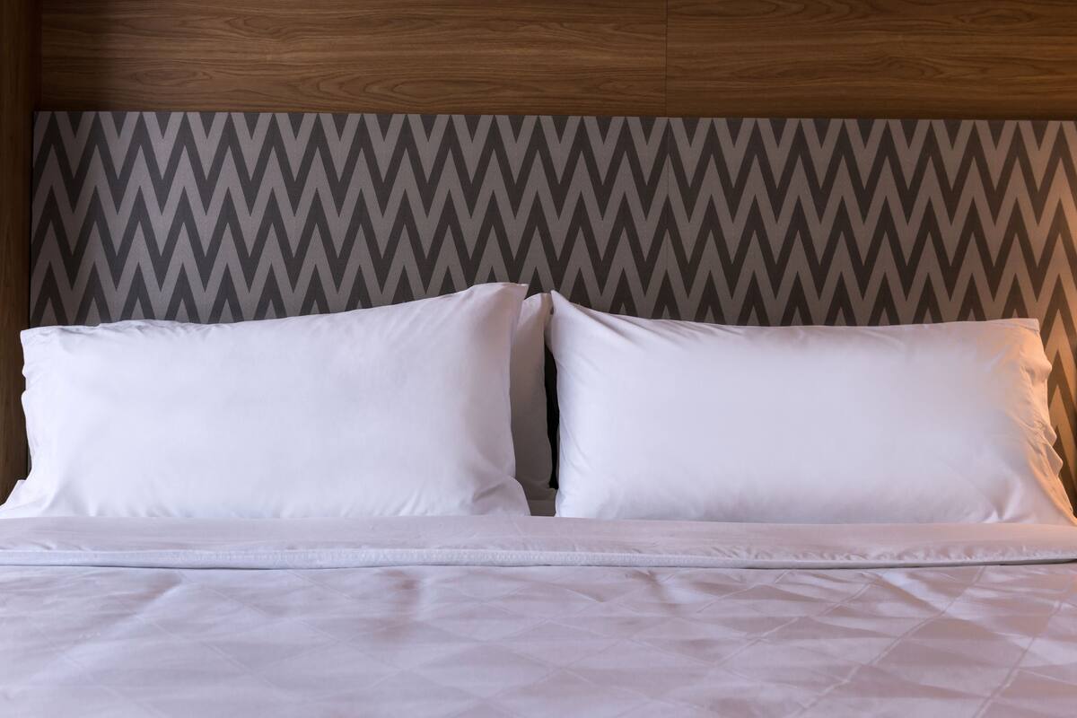 A neatly made bed with white bedding and a chevron-patterned headboard.