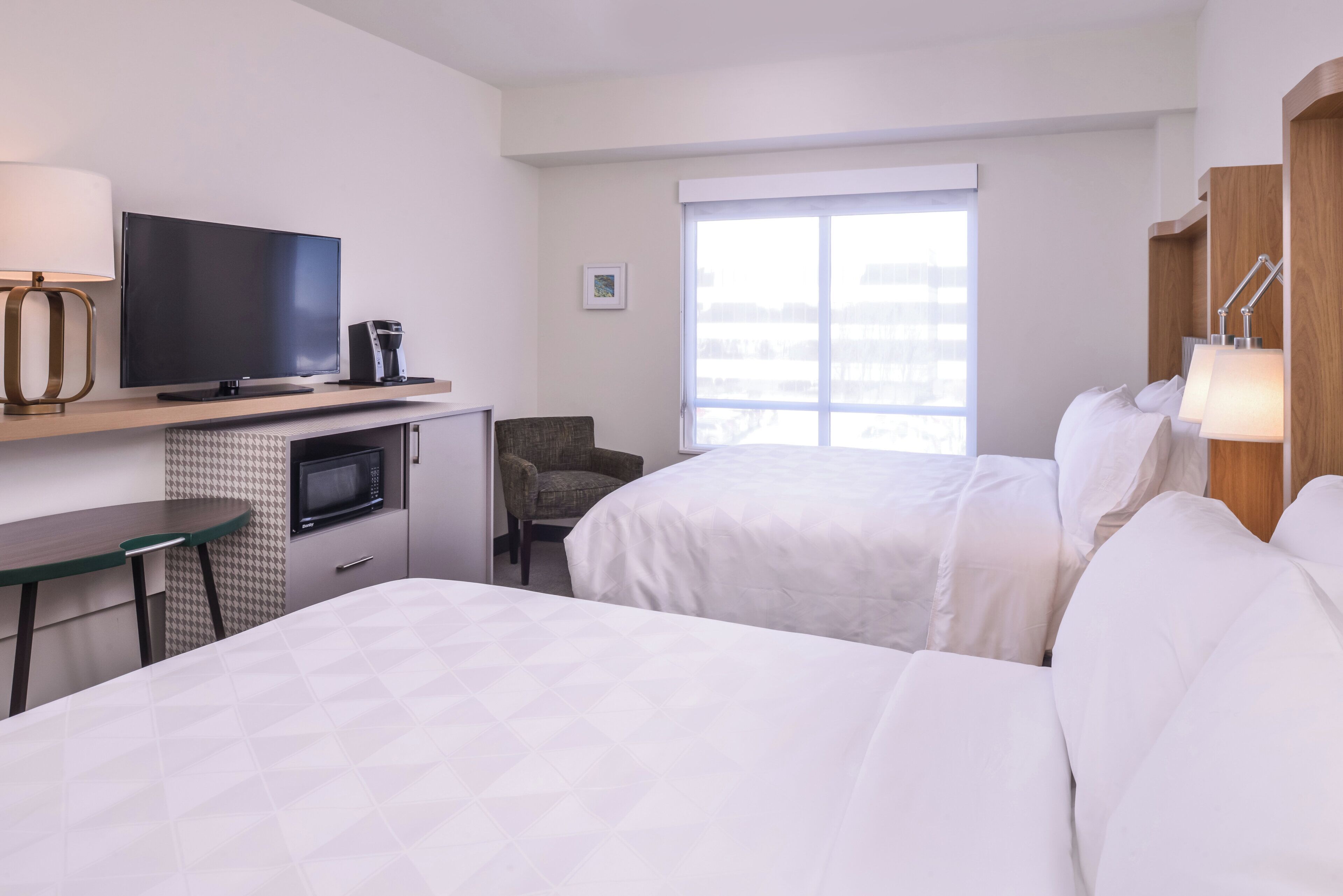 Een hotelkamer met twee bedden, een televisie, een bureau met een lamp, een stoel, een magnetron en een raam met uitzicht.