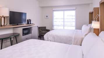 Habitación de hotel con dos camas, televisor, escritorio con lámpara, silla, microondas y ventana con vistas.