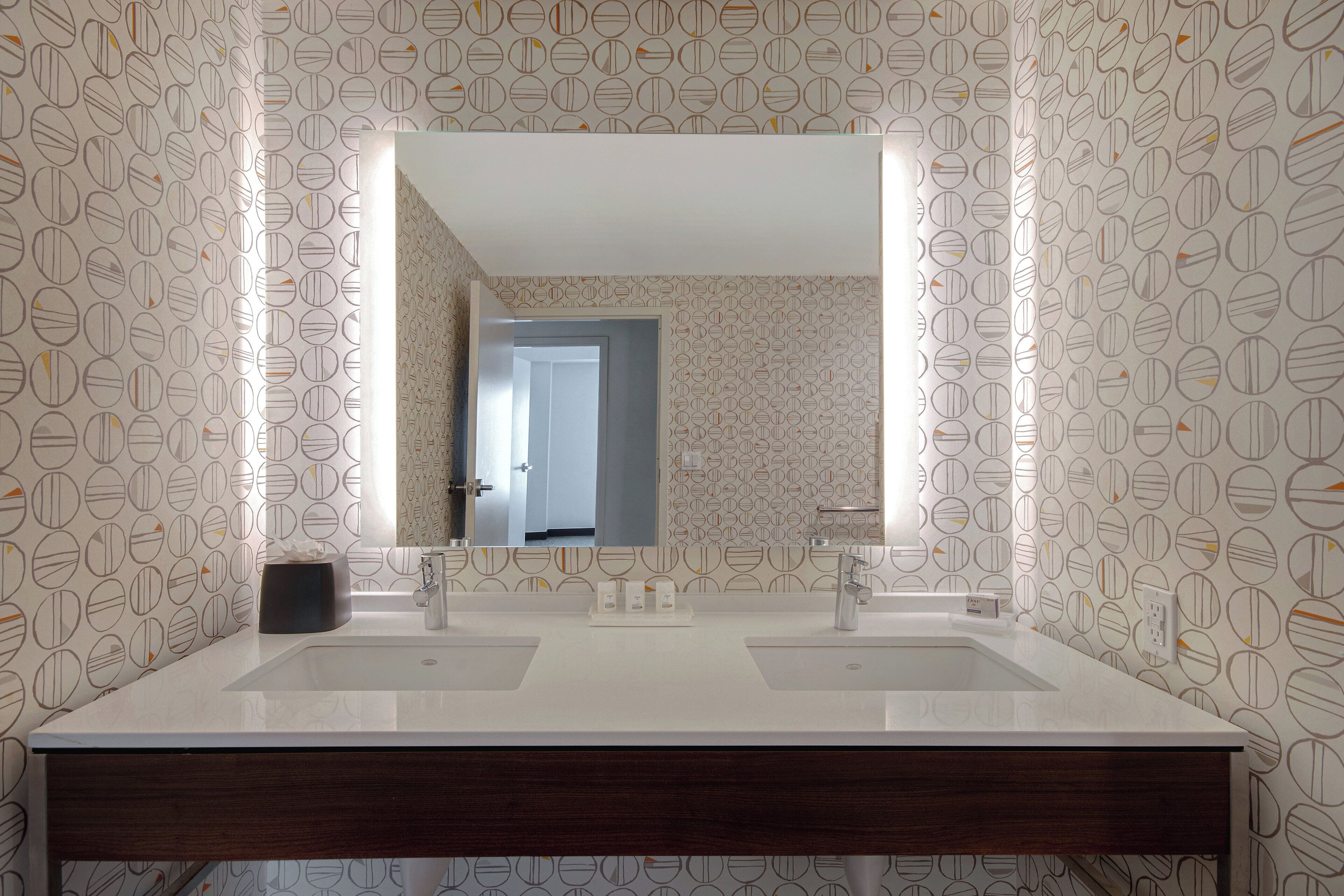 A bathroom with two sinks, a mirror, and patterned wallpaper.