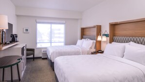 A hotel room with two beds, a desk with a coffee maker, a chair, and a window.