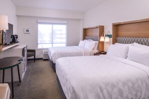 Une chambre d’hôtel avec deux lits, un bureau avec une machine à café, une chaise et une fenêtre.