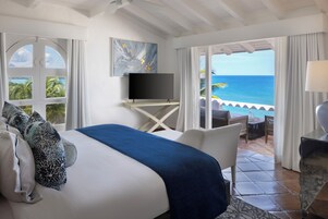 Een hotelkamer met een bed, een televisie, een balkon met uitzicht op zee en een zithoek met een tafel en stoelen.
