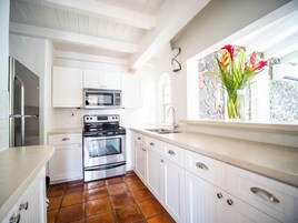 A kitchen with white cabinets, a stainless steel refrigerator, a microwave, an oven, and a window with a stone wall and a vase of flowers.