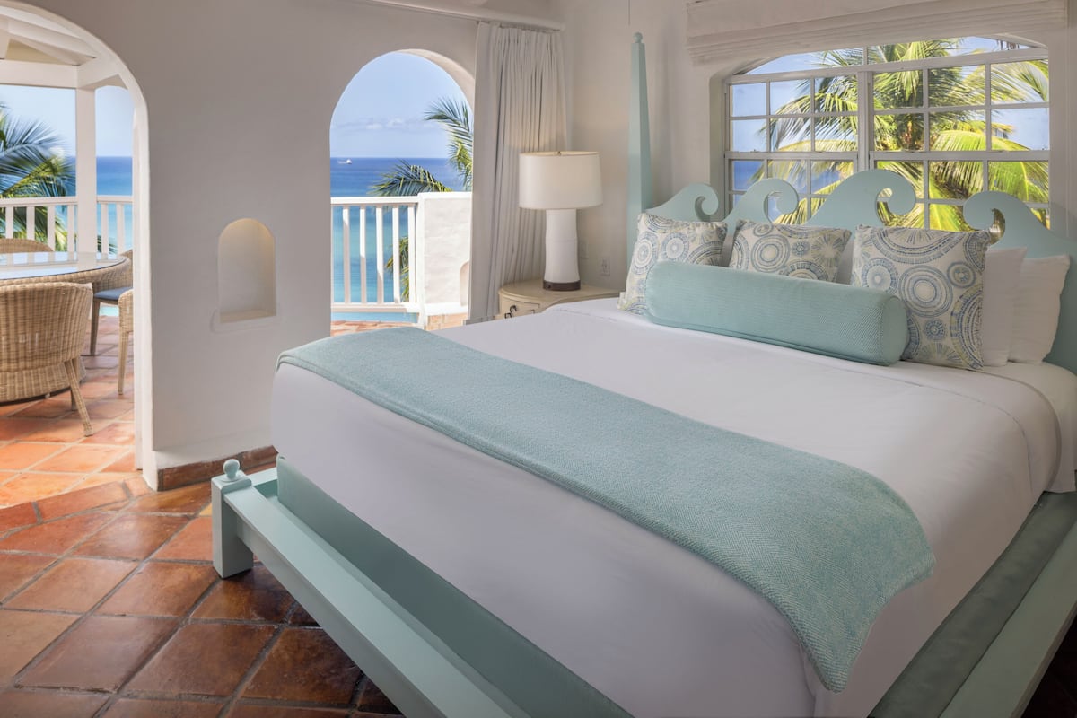 A bedroom with a large bed, a view of the ocean, and a balcony with wicker furniture.