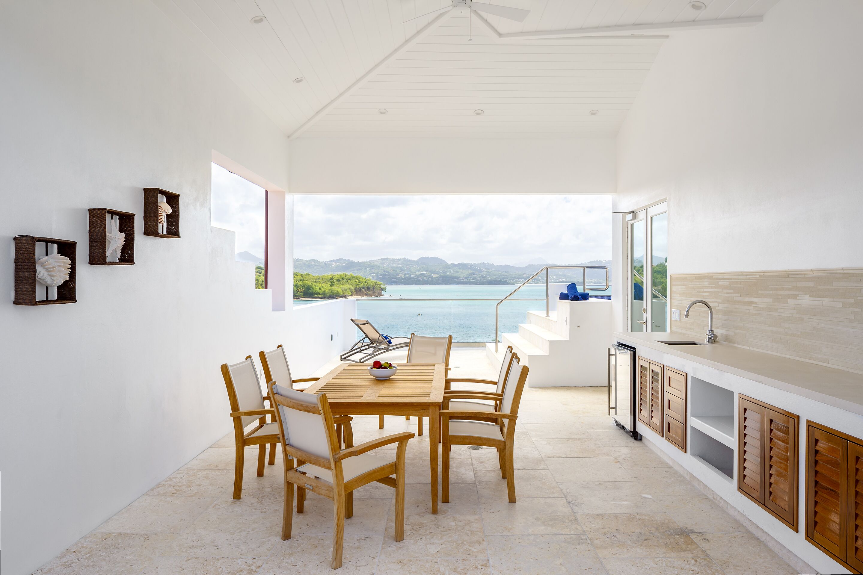 A modern kitchen with a large island, a dining area with wooden chairs, and a view of the sea.