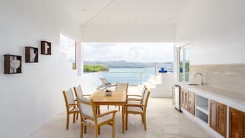 A modern kitchen with a large island, a dining area with wooden chairs, and a view of the sea.