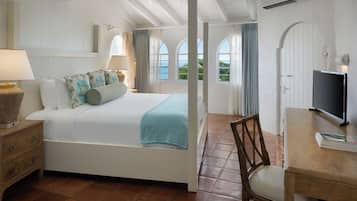 A bedroom with a bed, bedside table, chair, TV, and windows with curtains.