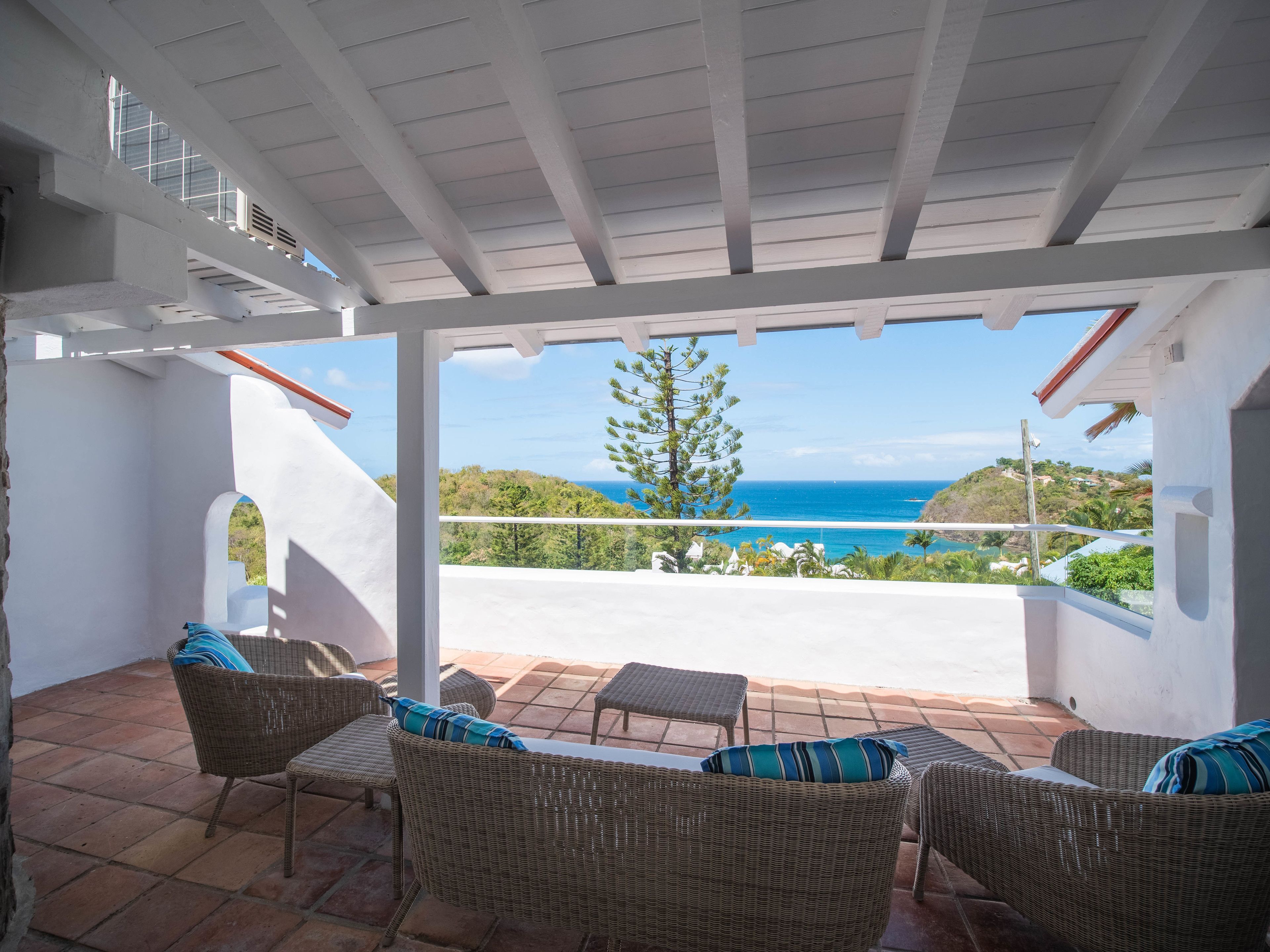 A covered patio with wicker furniture and a view of the ocean.