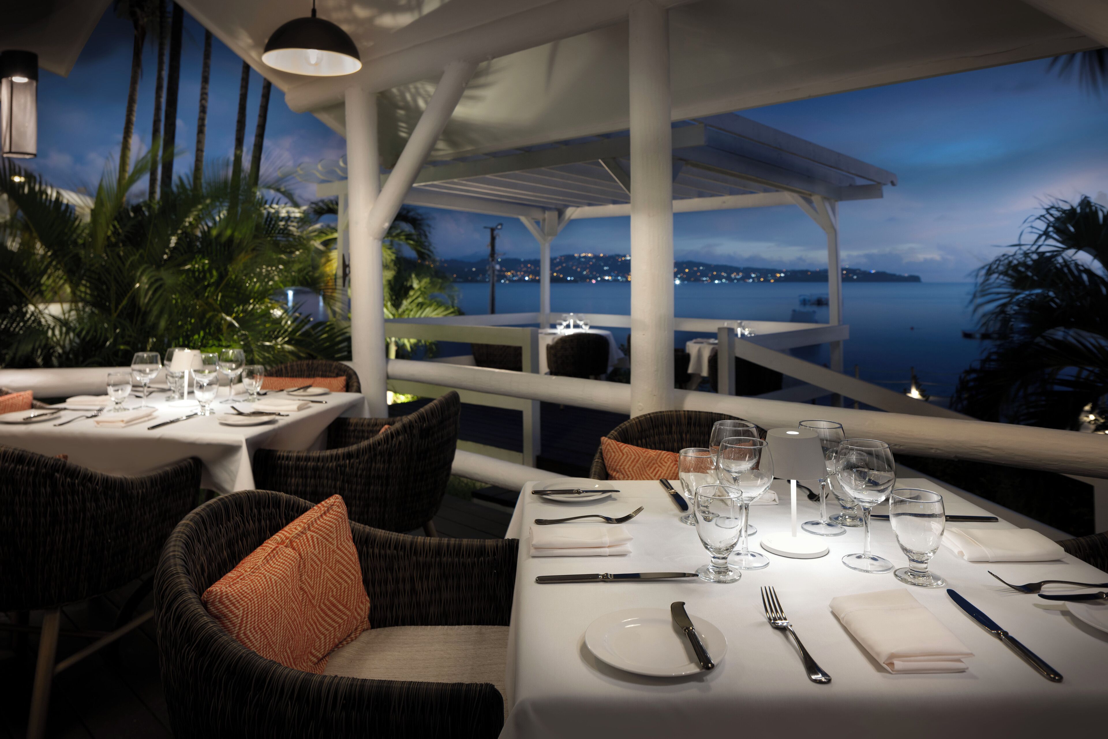 A restaurant with tables set for dining, overlooking a body of water at dusk.