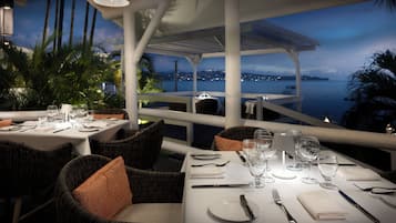 A restaurant with tables set for dining, overlooking a body of water at dusk.