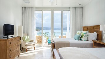 Hotelkamer met een grote schuifglazen deur naar een balkon met uitzicht op zee en bergen. Er is een bed, een bureau met een lamp en een televisie op een dressoir.