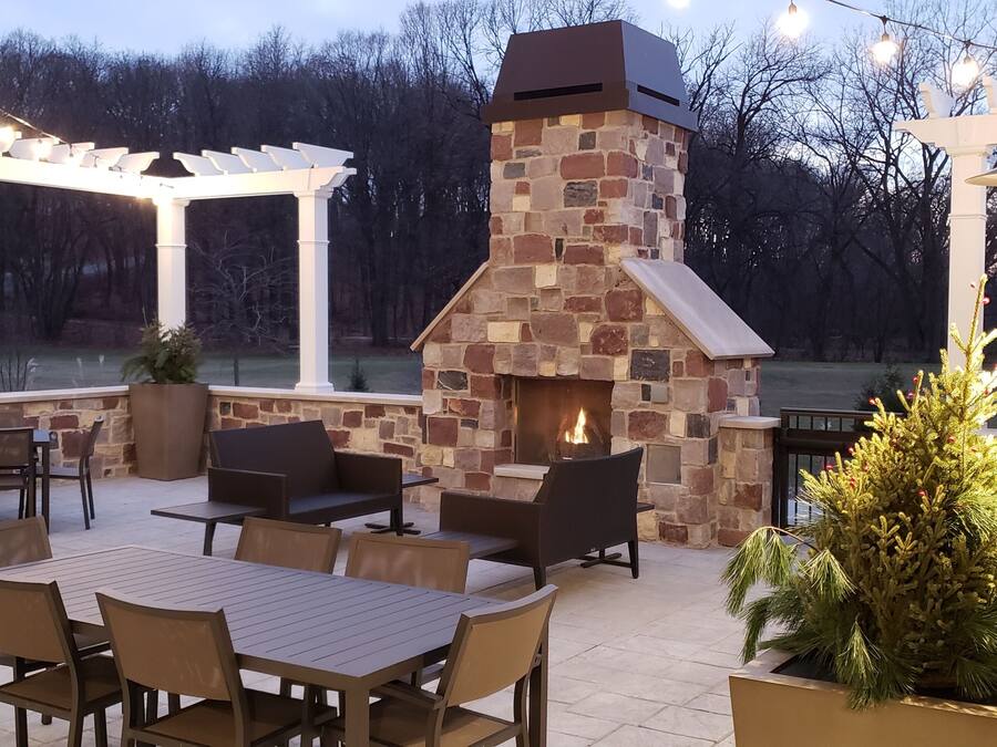 An outdoor patio with a stone fireplace, seating, and string lights.