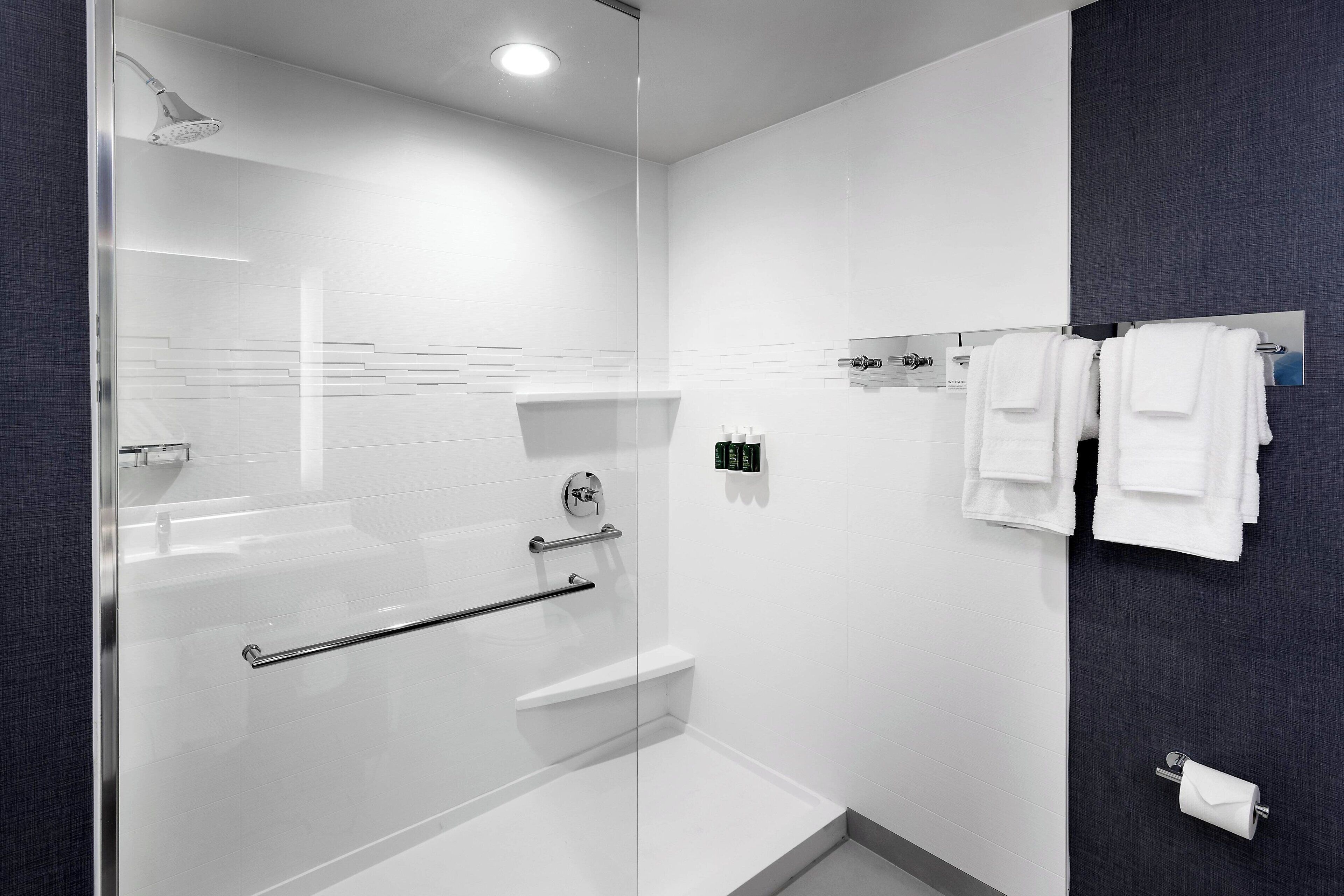 A modern bathroom with a glass-enclosed shower, a white bathtub, and a towel rack with towels.