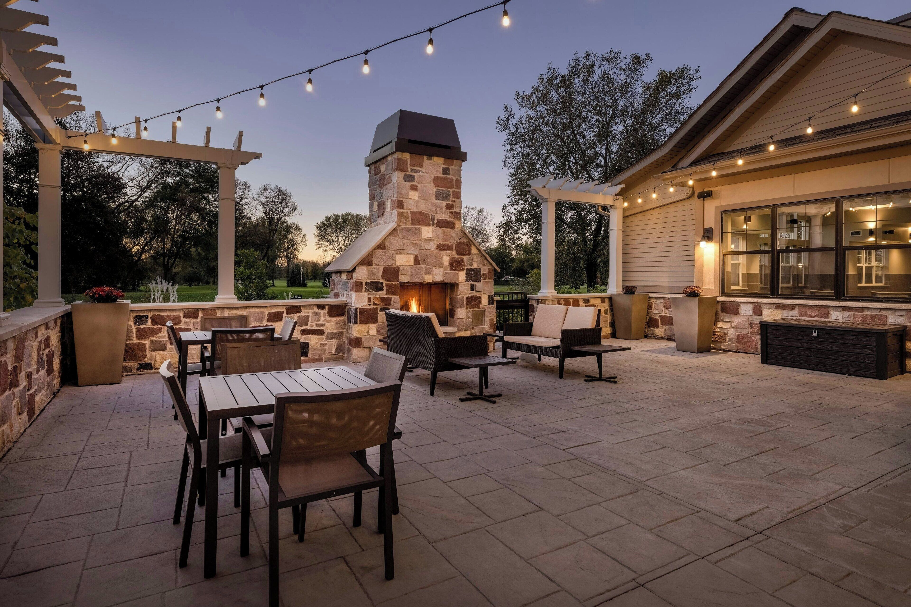 An outdoor patio with stone-built barbecue, seating, and string lights.